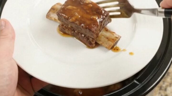 Slow cooker beef short ribs in a glossy chipotle honey barbecue sauce, garnished with fresh herbs.