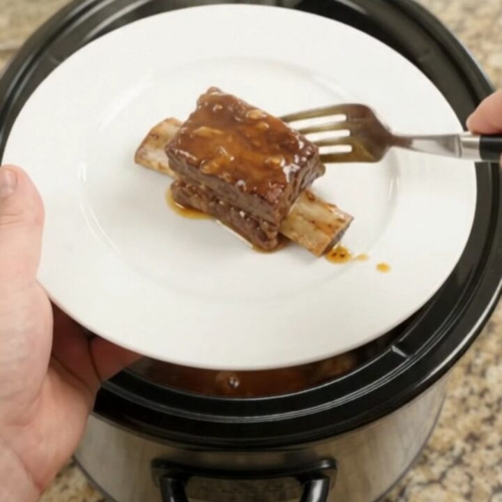 Slow cooker beef short ribs in a glossy chipotle honey barbecue sauce, garnished with fresh herbs.