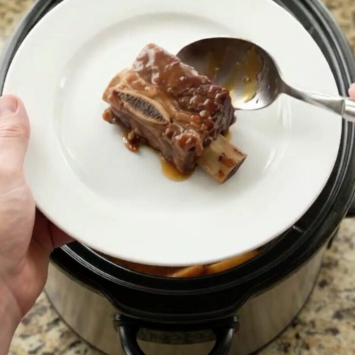 Slow cooker cherry cola BBQ short ribs glistening with sticky sauce, garnished with fresh cherries