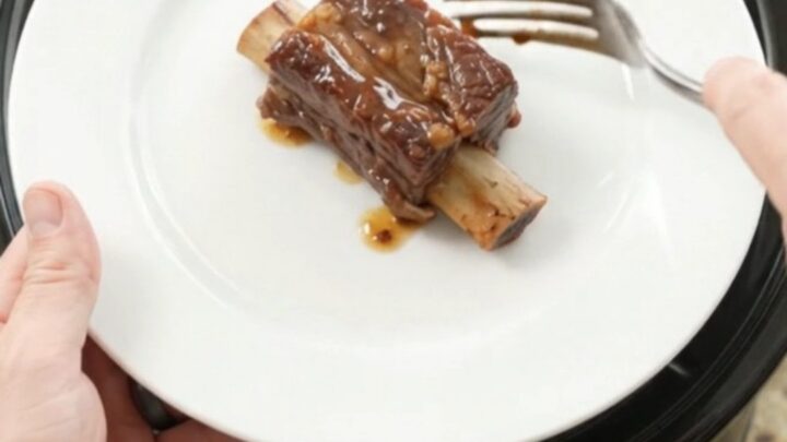 Slow-cooked beef short ribs glistening with cherry-cola barbecue sauce in a black crockpot