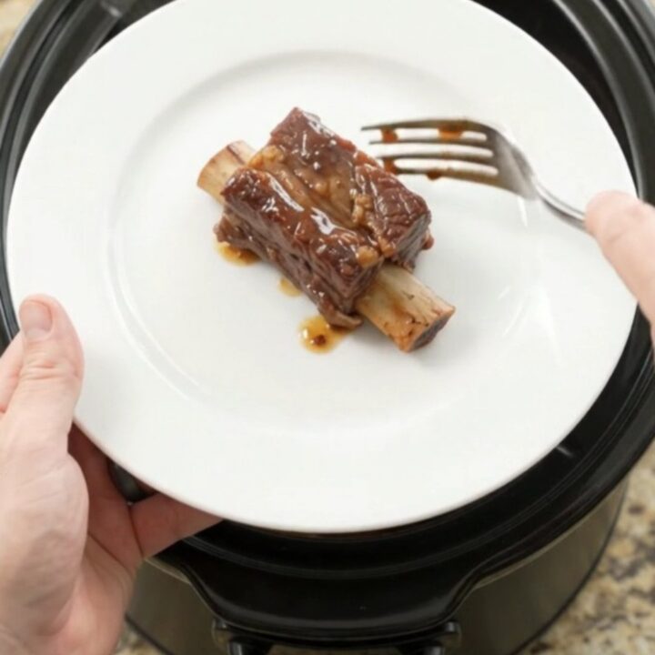 Slow-cooked beef short ribs glistening with cherry-cola barbecue sauce in a black crockpot
