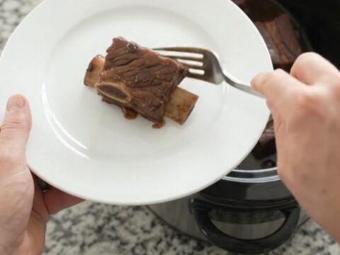Glossy slow-cooked beef short ribs with dark cherry cola sauce in a black crockpot