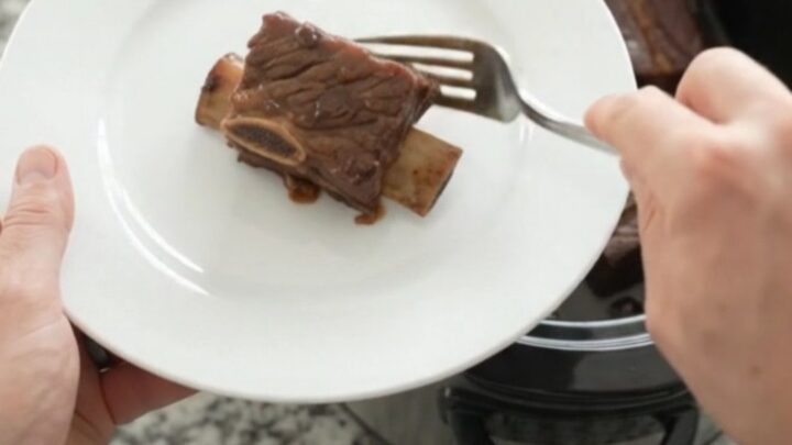 Glossy slow-cooked beef short ribs with dark cherry cola sauce in a black crockpot