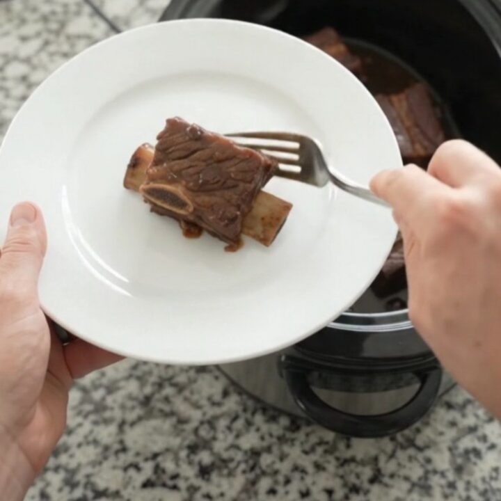Glossy slow-cooked beef short ribs with dark cherry cola sauce in a black crockpot