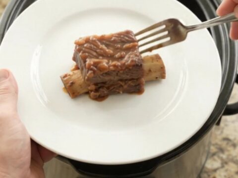Glossy BBQ short ribs in a black slow cooker, garnished with rosemary