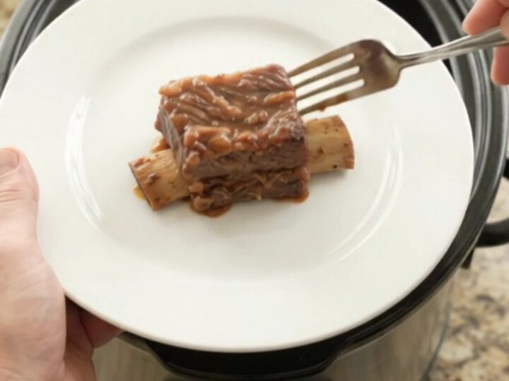 Glossy BBQ short ribs in a black slow cooker, garnished with rosemary