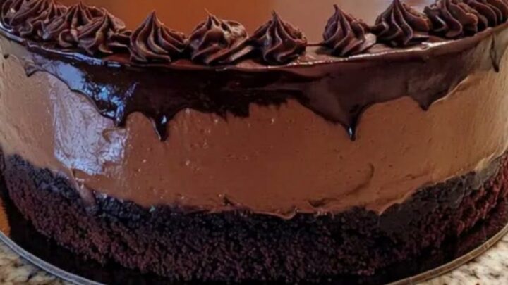 A decadent layered chocolate mousse cake with glossy ganache and piped rosettes on a granite surface.