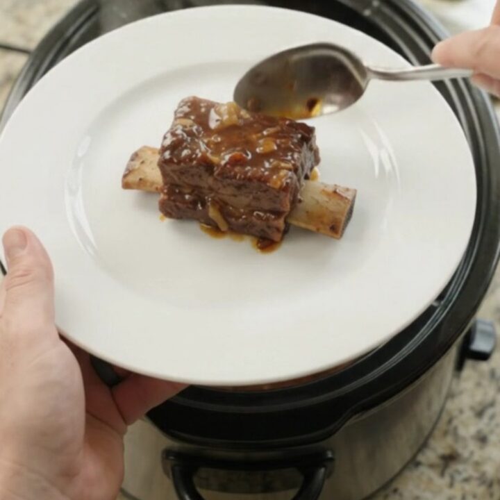 Glossy slow-cooked beef short ribs in a dark molasses BBQ sauce in a black crockpot