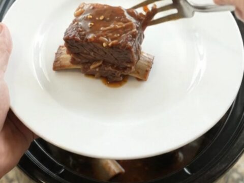 Slow cooker beef short ribs glazed in barbecue sauce, garnished with fresh herbs
