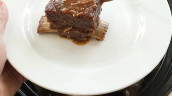 Slow cooker beef short ribs glazed in barbecue sauce, garnished with fresh herbs