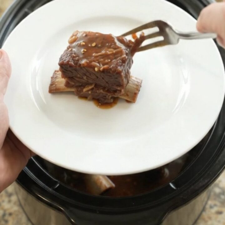 Slow cooker beef short ribs glazed in barbecue sauce, garnished with fresh herbs