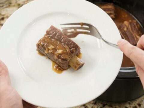 Bone-in beef short ribs glazed in a glossy maple bourbon BBQ sauce, served on a white plate with extra sauce spooned over.