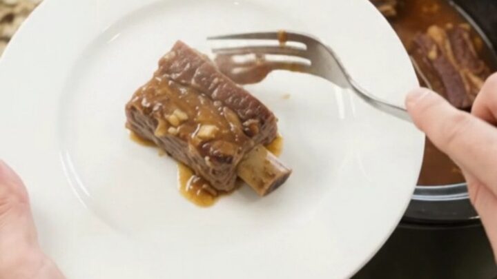 Bone-in beef short ribs glazed in a glossy maple bourbon BBQ sauce, served on a white plate with extra sauce spooned over.