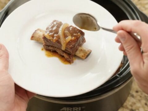 Glossy beef short ribs in a slow cooker with sticky barbecue sauce and caramelized onions
