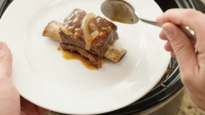 Glossy beef short ribs in a slow cooker with sticky barbecue sauce and caramelized onions