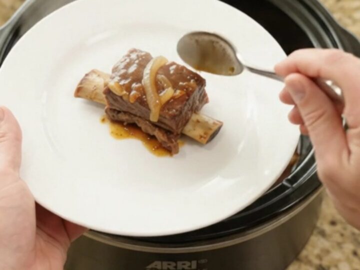 Glossy beef short ribs in a slow cooker with sticky barbecue sauce and caramelized onions
