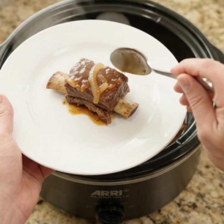 Glossy beef short ribs in a slow cooker with sticky barbecue sauce and caramelized onions