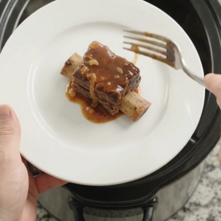 A pile of glistening BBQ short ribs on a white plate, garnished with caramelized onions