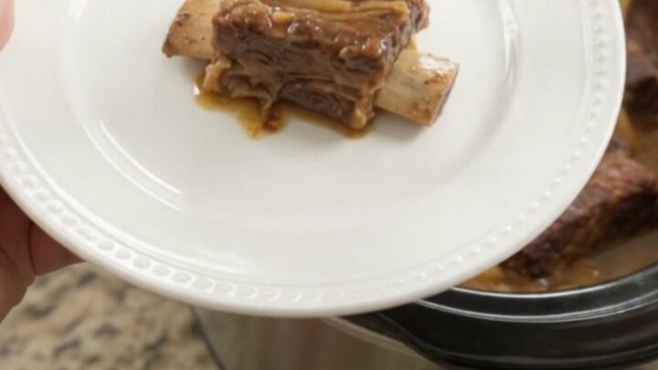 Glazed beef short ribs with caramelized onions in a slow cooker, topped with maple bourbon BBQ sauce.