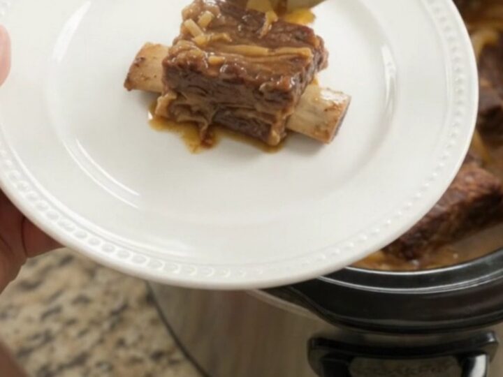 Glazed beef short ribs with caramelized onions in a slow cooker, topped with maple bourbon BBQ sauce.