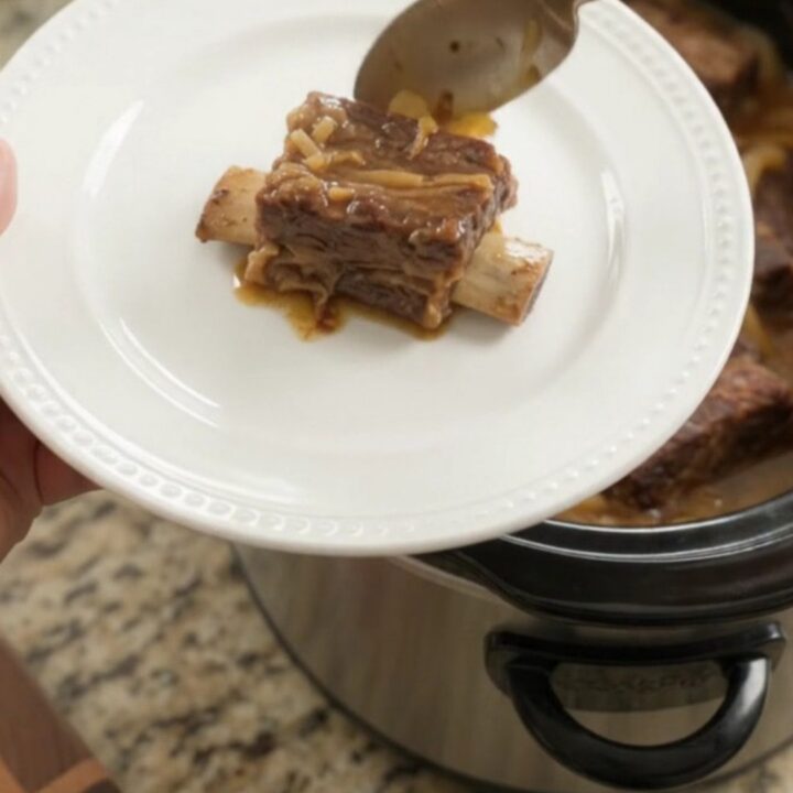 Glazed beef short ribs with caramelized onions in a slow cooker, topped with maple bourbon BBQ sauce.