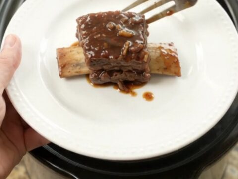 A slow cooker filled with glossy, dark beef short ribs in a rich molasses sauce, topped with caramelized onions.