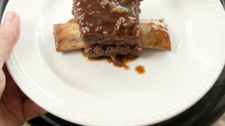 A slow cooker filled with glossy, dark beef short ribs in a rich molasses sauce, topped with caramelized onions.