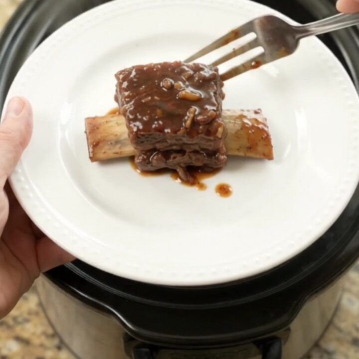 A slow cooker filled with glossy, dark beef short ribs in a rich molasses sauce, topped with caramelized onions.