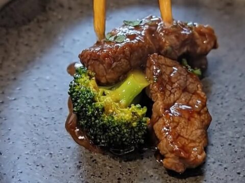A dark ceramic plate featuring glistening, sauce-coated flank steak and vibrant green broccoli florets.