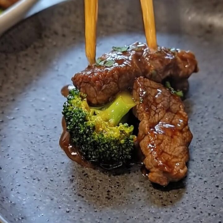 A dark ceramic plate featuring glistening, sauce-coated flank steak and vibrant green broccoli florets.