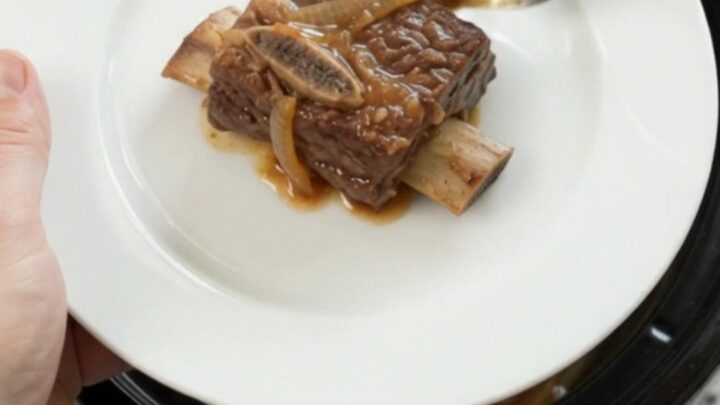 Glazed beef short ribs in a black Crockpot, covered in honey hickory BBQ sauce and caramelized onions.
