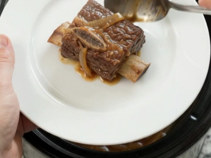 Glazed beef short ribs in a black Crockpot, covered in honey hickory BBQ sauce and caramelized onions.