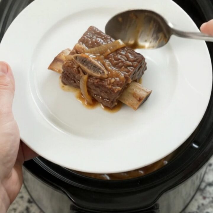 Glazed beef short ribs in a black Crockpot, covered in honey hickory BBQ sauce and caramelized onions.