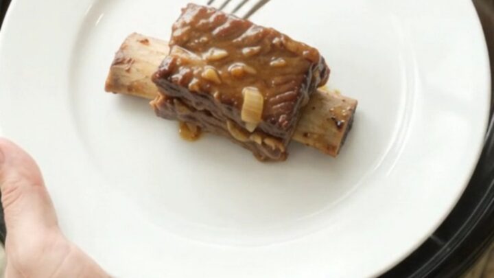 Beef short ribs in a crockpot, glazed with dark barbecue sauce and topped with caramelized onions.