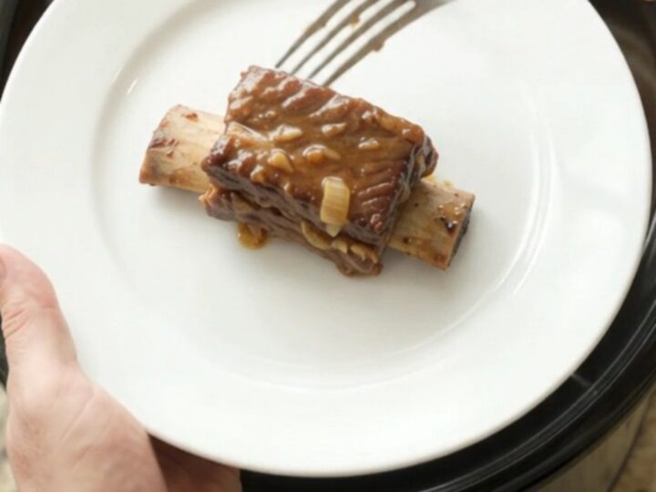 Beef short ribs in a crockpot, glazed with dark barbecue sauce and topped with caramelized onions.