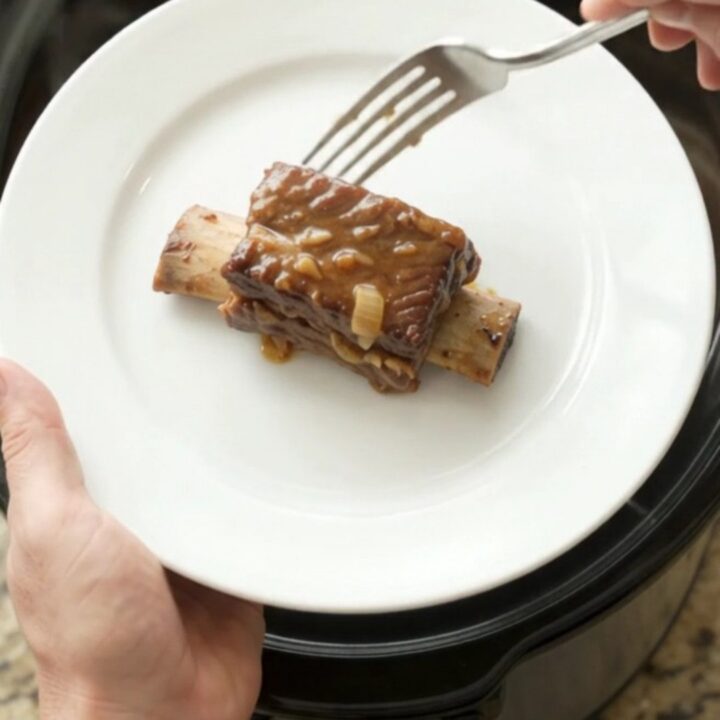 Beef short ribs in a crockpot, glazed with dark barbecue sauce and topped with caramelized onions.