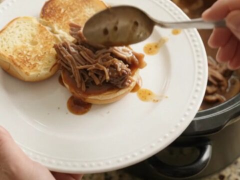 Shredded beef chuck roast in a slow cooker with mushrooms and brown gravy