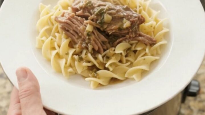 Shredded beef chuck roast in a slow cooker with rich gravy and butter slices