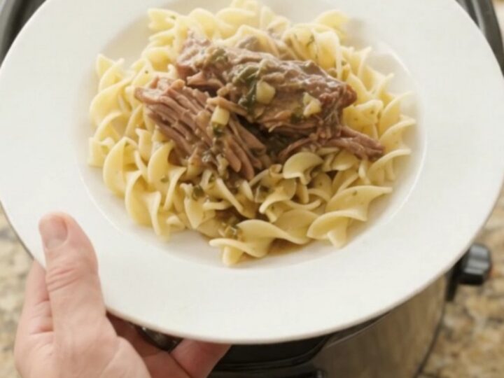 Shredded beef chuck roast in a slow cooker with rich gravy and butter slices