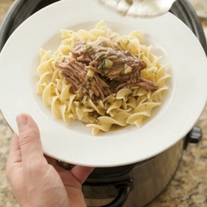 Shredded beef chuck roast in a slow cooker with rich gravy and butter slices