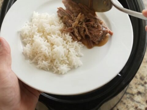 Slow cooker chuck roast with creamy Dijon gravy, shredded and piled on a white plate with rice.