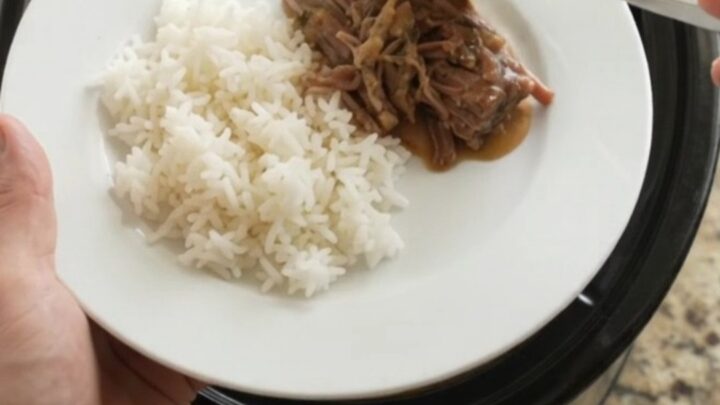 Slow cooker chuck roast with creamy Dijon gravy, shredded and piled on a white plate with rice.