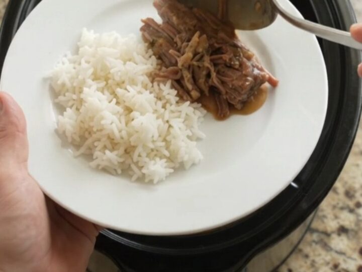 Slow cooker chuck roast with creamy Dijon gravy, shredded and piled on a white plate with rice.