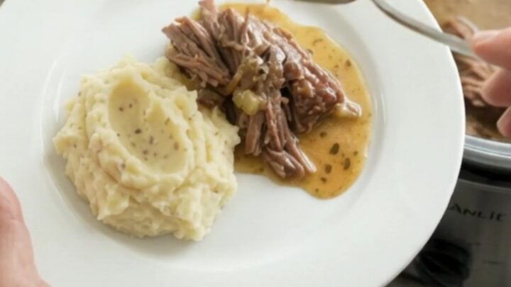 Shredded beef chuck roast with gravy in a slow cooker, topped with butter
