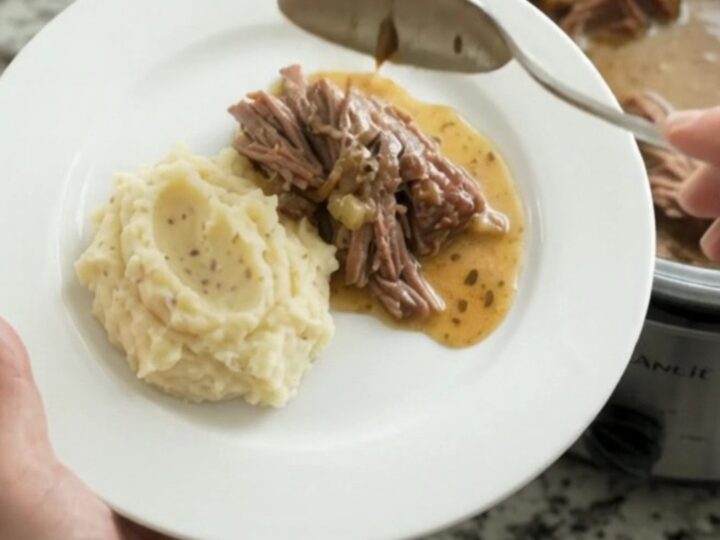 Shredded beef chuck roast with gravy in a slow cooker, topped with butter