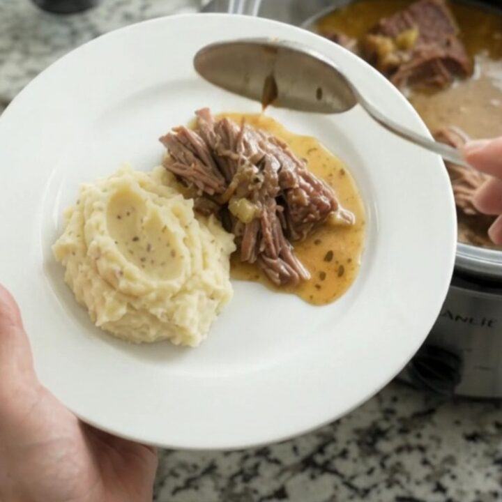Shredded beef chuck roast with gravy in a slow cooker, topped with butter
