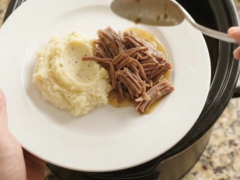 Slow-cooker Guinness onion butter chuck roast in a black crockpot, with pearl onions and glossy sauce.
