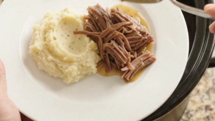 Slow-cooker Guinness onion butter chuck roast in a black crockpot, with pearl onions and glossy sauce.