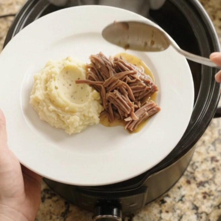 Slow-cooker Guinness onion butter chuck roast in a black crockpot, with pearl onions and glossy sauce.