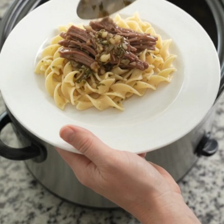 Shredded beef chuck roast with pearl onions in a rich stout gravy in a slow cooker